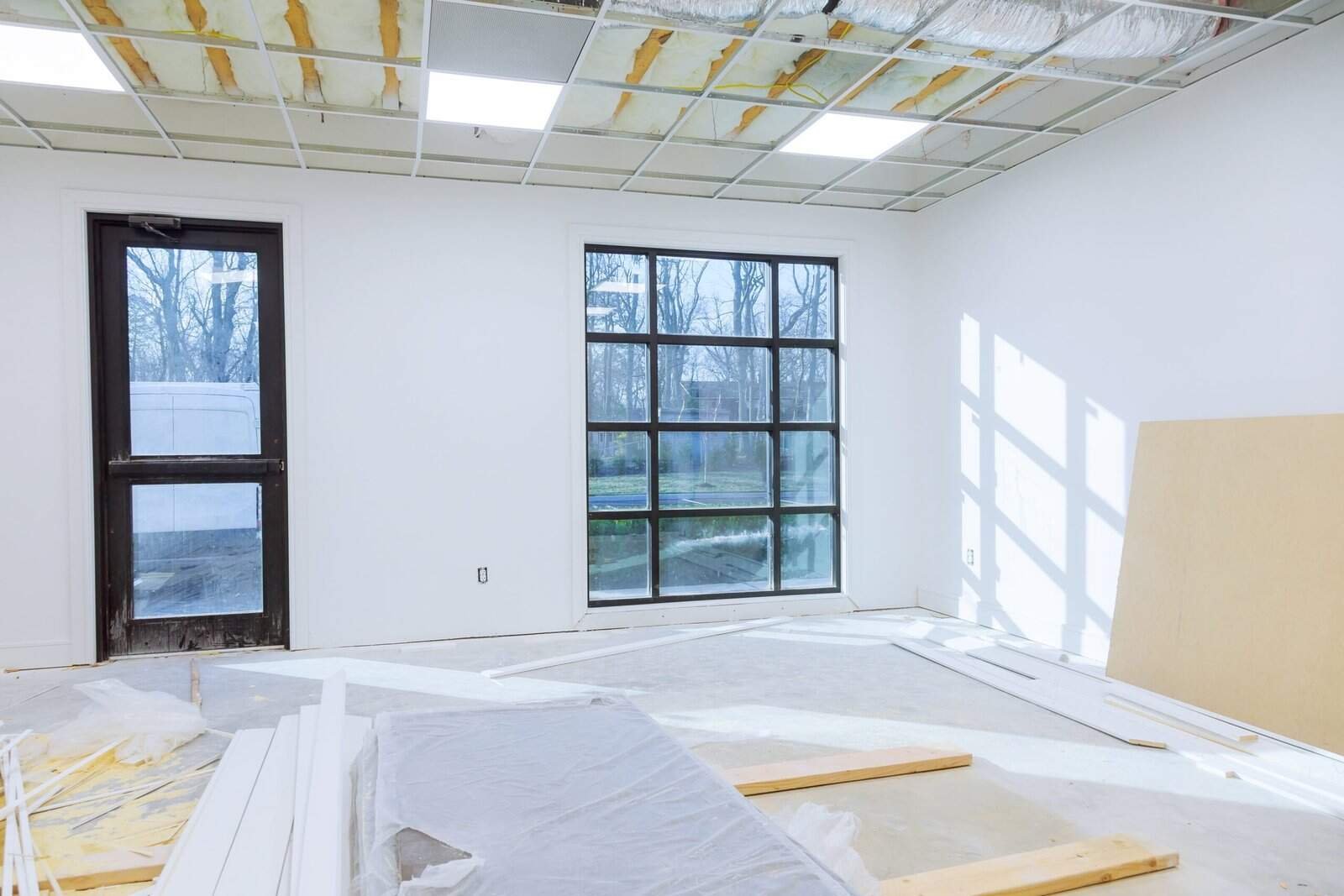 Bright white interior wall painting with large windows and construction materials, showcasing professional residential painting services.